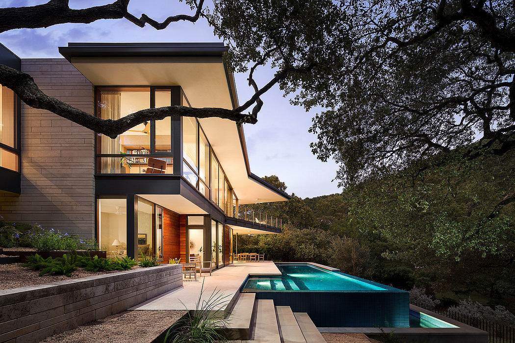 Striking modern architecture featuring sleek glass facades, a pool, and lush landscaping.
