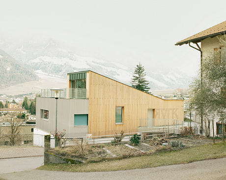 Modern wooden facade with large windows, set against a snowy mountain backdrop.