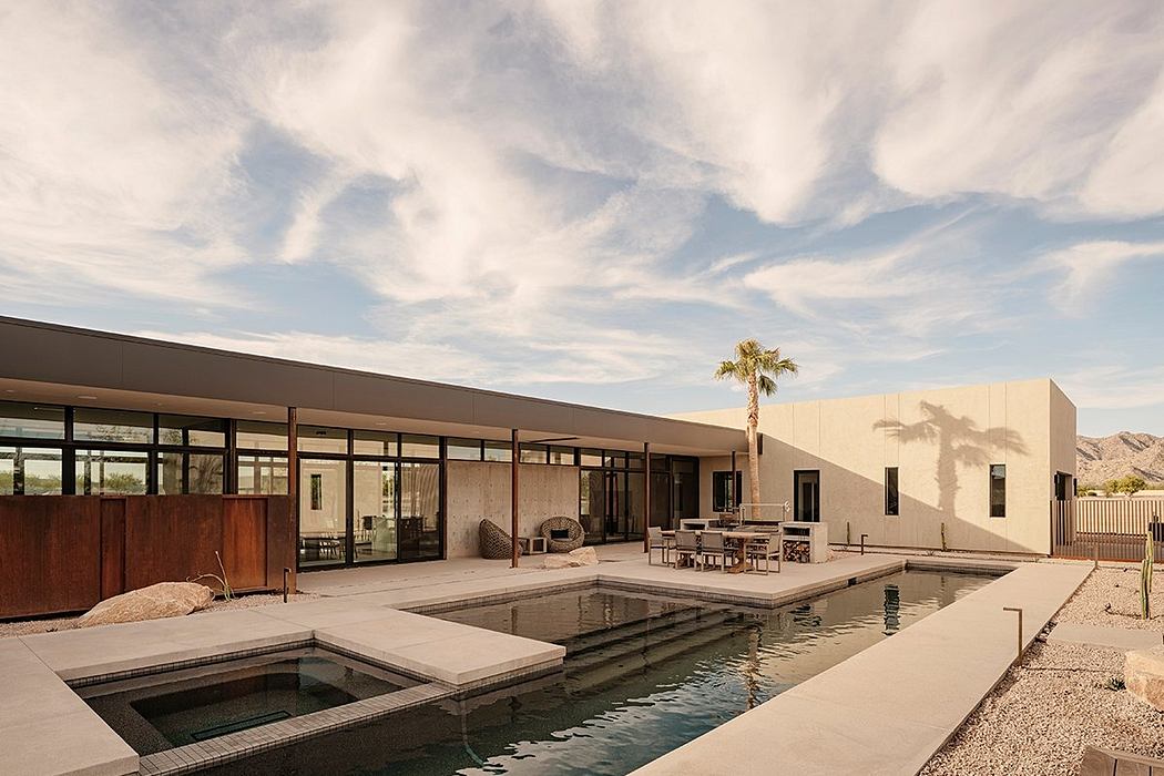 A modern desert house with a pool, surrounded by mountains and a palm tree.