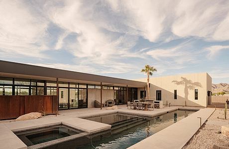 A modern desert house with a pool, surrounded by mountains and a palm tree.