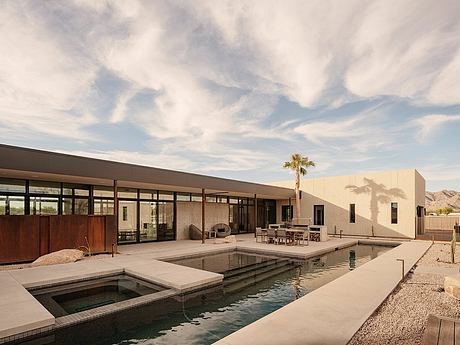 A modern desert house with a pool, surrounded by mountains and a palm tree.