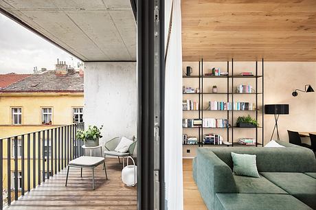 Modern apartment interior with open balcony, concrete walls, and wooden flooring. Stylish shelving unit and plush sofa.