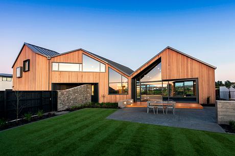 Modern multi-level home with wooden exterior, expansive windows, and patio area.