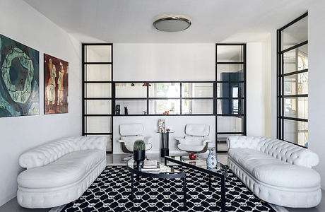 Modern living room with white Chesterfield-style sofas, black geometric rug, and metal shelving.