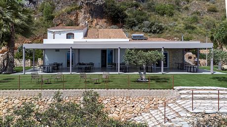 Modern Mediterranean-style villa with covered patio, manicured lawn, and stone retaining wall.