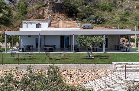 Modern Mediterranean-style villa with covered patio, manicured lawn, and stone retaining wall.