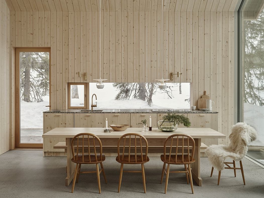 Rustic wood-paneled kitchen with large window overlooking snowy forest, wooden chairs.