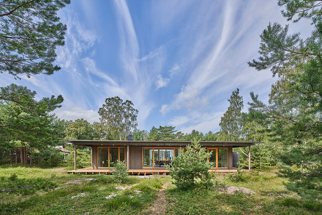 A modern, single-story cabin with large windows and a wooden exterior, surrounded by lush greenery.