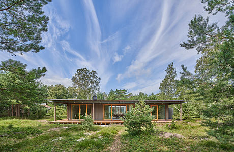 A modern, single-story cabin with large windows and a wooden exterior, surrounded by lush greenery.