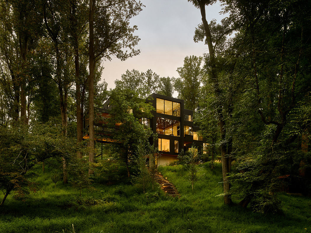 A modern, multi-level glass and wood home nestled in a dense, lush forest.