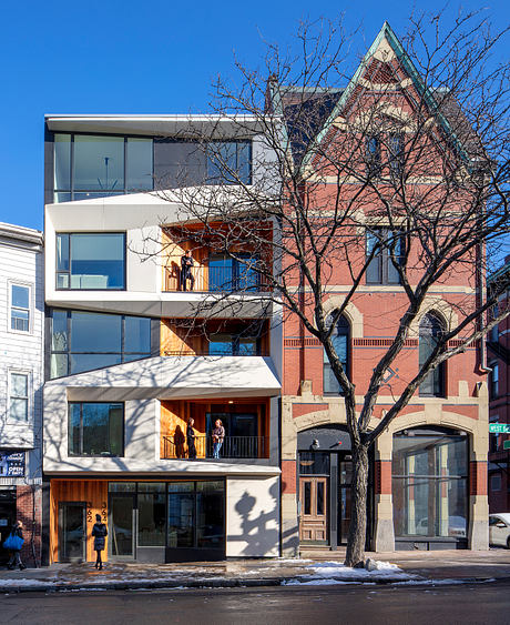 A modern building with glass walls, balconies, and a historic brick structure in the background.