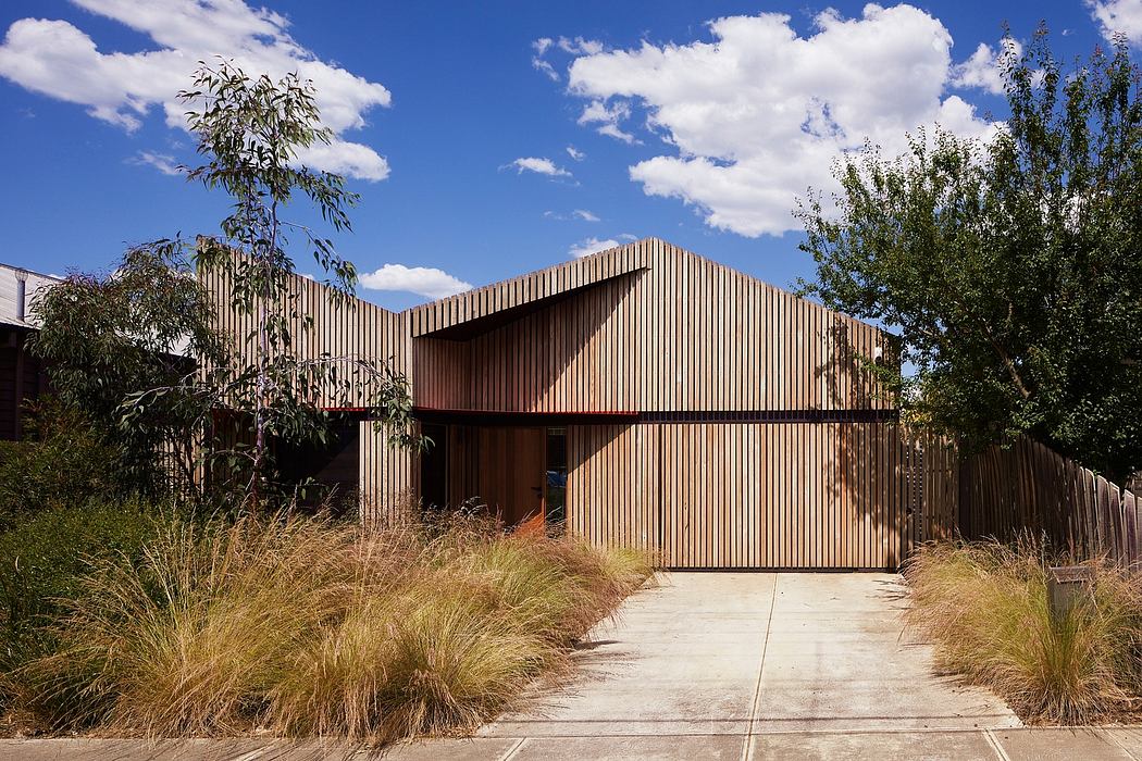 A modern, wooden-slatted house set amidst lush greenery and a paved walkway.