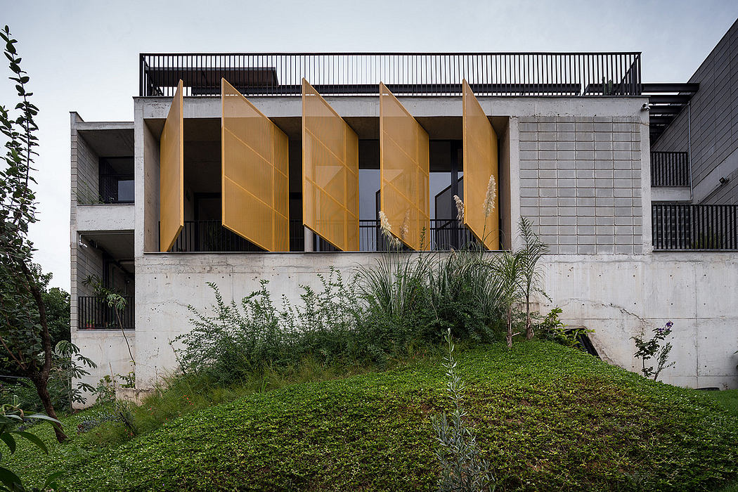 A modern concrete building with yellow angled panels forming a facade, surrounded by vegetation.