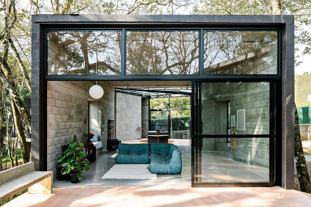 A modern, glass-walled home nestled in lush greenery, with a cozy seating area and minimalist decor.