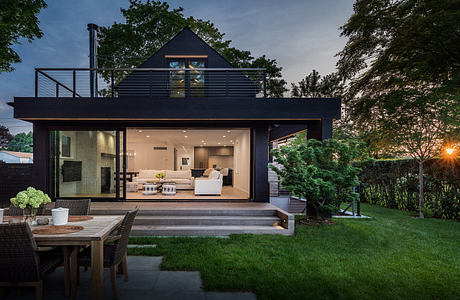 Contemporary architectural design with large glass doors, dark exterior, and surrounding greenery.