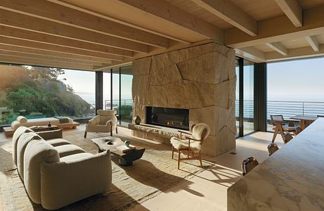 Cozy living space with wooden beams, large stone fireplace, and panoramic ocean views.