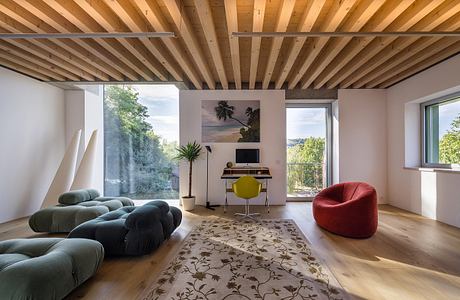 Warm-toned wooden ceiling beams, large windows, plush seating, and a tropical-themed wall art.