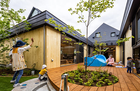 A modern outdoor play area with wooden structures, greenery, and a tent for children.