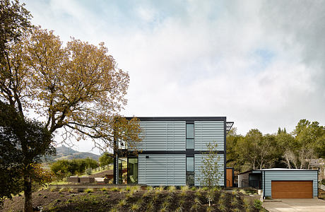 Modern, sleek home with large windows, wood accents, and a surrounding garden in a wooded setting.