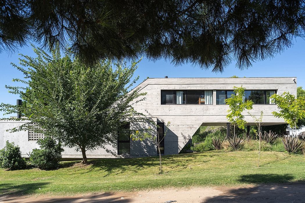 Modern two-story concrete house with large windows and trees surrounding it.