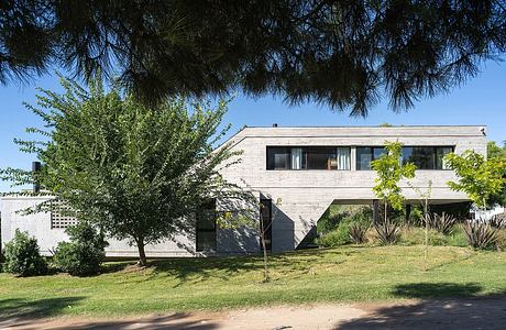 Modern two-story concrete house with large windows and trees surrounding it.