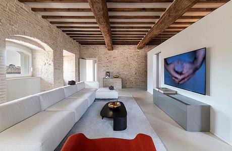 Spacious living room with exposed brick walls, wooden ceiling beams, and modern furnishings.