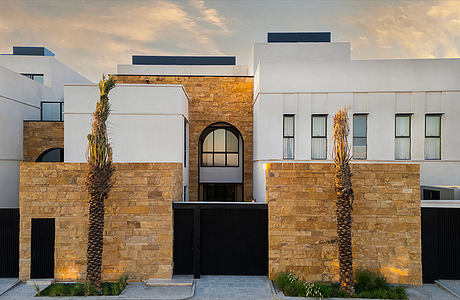 Striking modern architecture featuring stone walls, arched entryway, and palm trees.