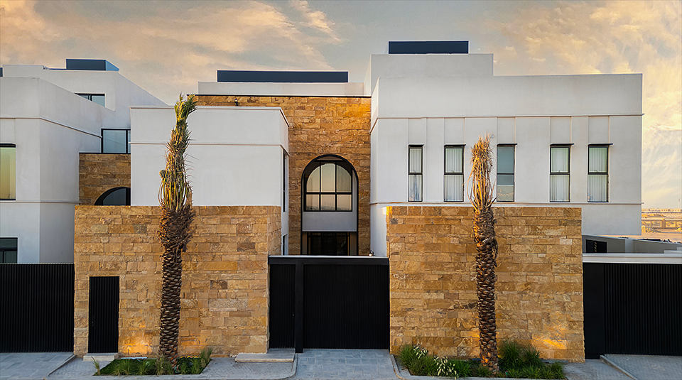 Striking modern architecture featuring stone walls, arched entryway, and palm trees.
