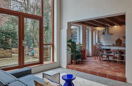 A cozy modern living room with large windows overlooking lush greenery and an open kitchen area.