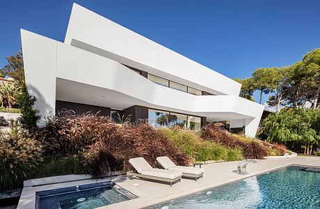 A modern, asymmetrical home with clean lines, a pool, and lush landscaping.