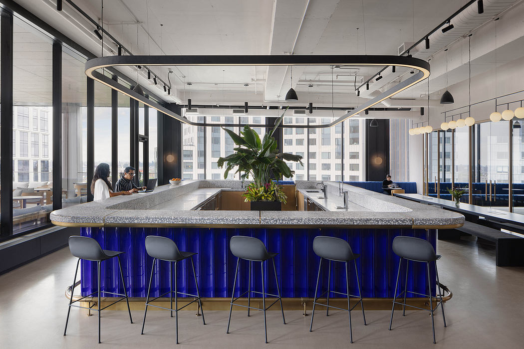 Modern open-plan office space with sleek granite bar, pendant lighting, and lush plant decor.
