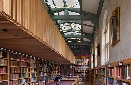 A grand, wood-paneled library with a vaulted glass ceiling and rows of bookshelves.