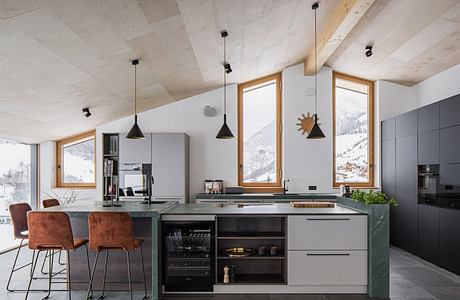 Modern kitchen with vaulted ceiling, wooden window frames, and black pendant lights.