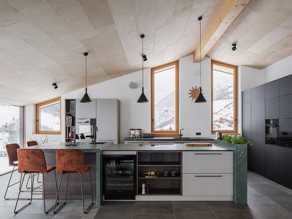 Modern kitchen with vaulted ceiling, wooden window frames, and black pendant lights.