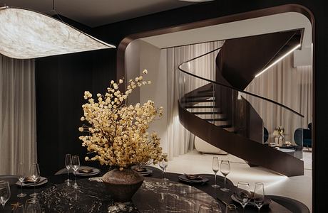 Elegant spiral staircase, marble table, and a striking floral centerpiece in a modern space.