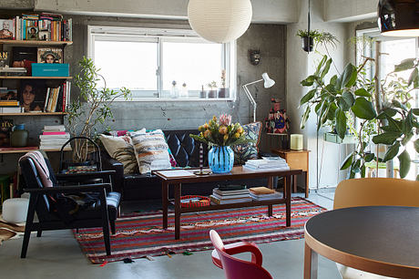 Cozy living room with textured concrete walls, leafy plants, and eclectic furnishings.