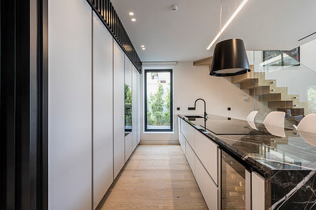 Modern kitchen with sleek cabinetry, black marble countertops, and a glass window overlooking greenery.