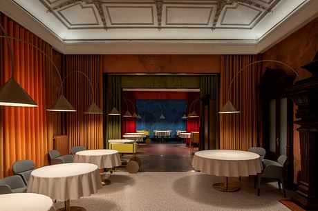 A lavish, ornately decorated room with a coffered ceiling, dramatic curtains, and chic round tables.