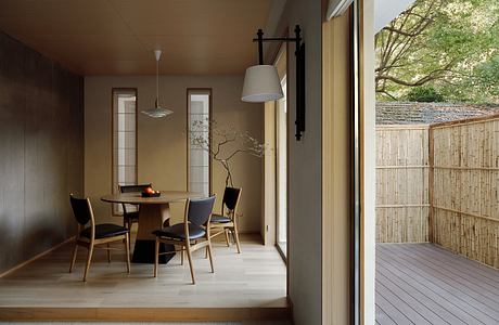 Warm, minimal dining area with wooden furniture, lighting, and sliding glass door to deck.