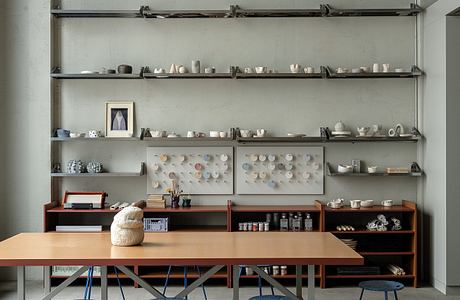 Minimalist workspace with open shelves, wooden table, and blue accent stools.