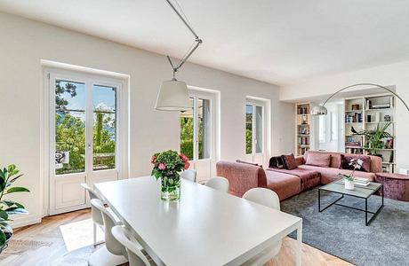 Bright and airy living room with modern furniture, large windows, and lush greenery outside.