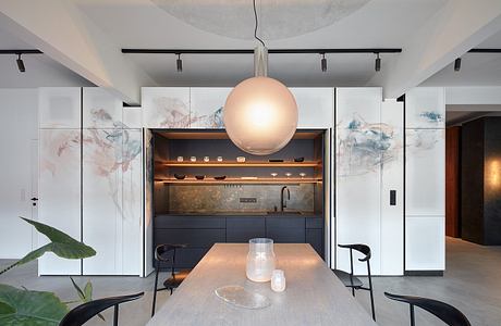 Minimalist open-plan kitchen with abstract wall panels, track lighting, and pendant globe.