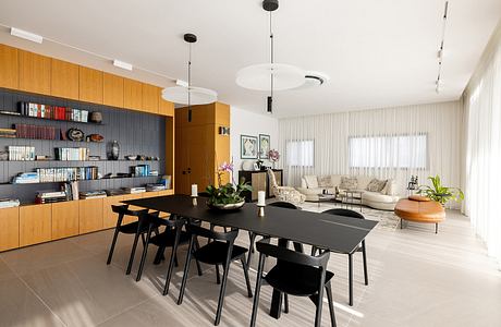 Minimalist dining area with sleek black furniture, illuminated by pendant lights and surrounded by wooden cabinetry.