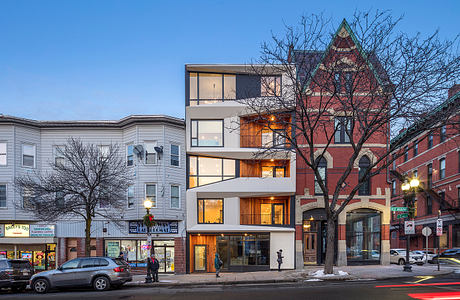 Striking modern apartment building with glass facades and brick accents, framed by bare trees.