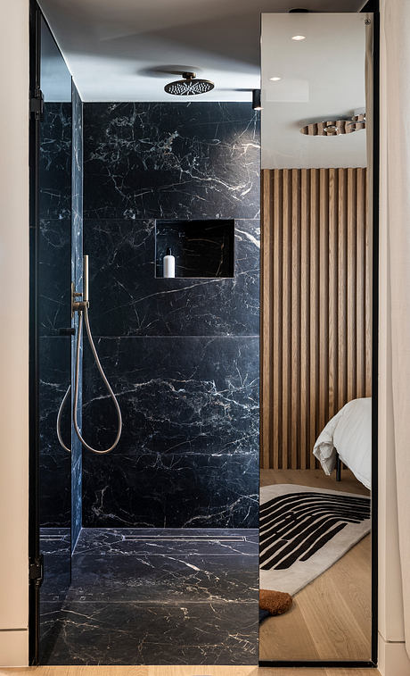 Modern bathroom with black marble walls, wooden slat accent, and rain shower head.