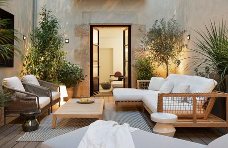 Cozy outdoor lounge area with wood furnishings, potted plants, and a view of a doorway.