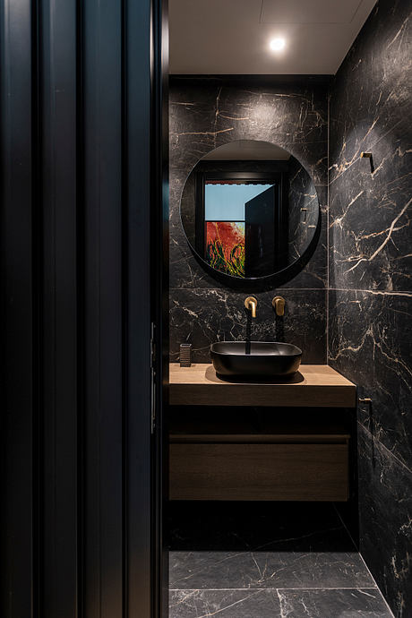 Sleek, modern powder room with dark marble walls, circular mirror, and wood vanity.