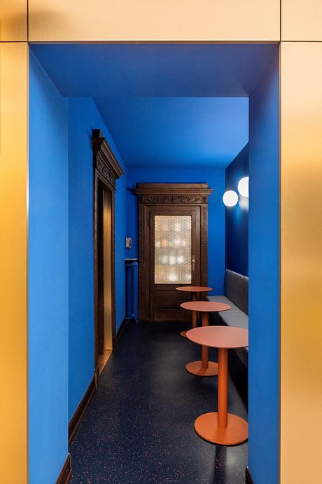 A vibrant blue room with a wooden cabinet and stylish orange bar stools, showcasing the architectural design.