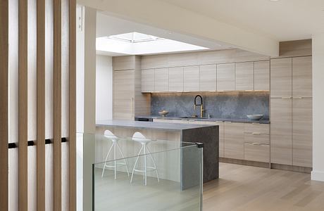 Minimalist kitchen design with wood-paneled cabinets, concrete countertops, and glass divider.