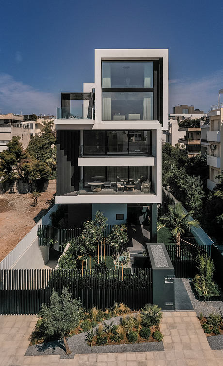 Four-story modern building with glass walls, terraces, and lush landscaping.